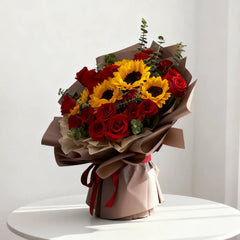 Sunflower and red rose bouquet for flower delivery, arranged in brown wrapping on a white table