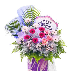 Grand opening flower stand with pink and red blooms, fern leaves, and Best Wishes sign for delivery