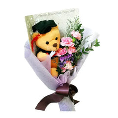 Graduation bouquet with pink carnations, foliage, and a teddy bear for flower delivery