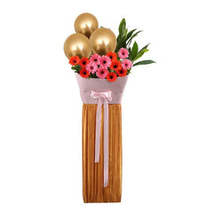 Flower delivery arrangement with pink and orange gerbera daisies, gold balloons, and greenery.