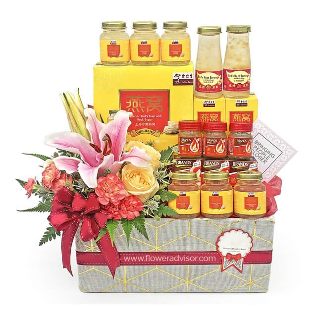 Flower delivery hamper with pink lilies, roses, and assorted health product jars.