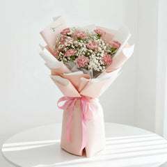 Pink carnation bouquet with baby’s breath, wrapped in pastel paper, for flower delivery.
