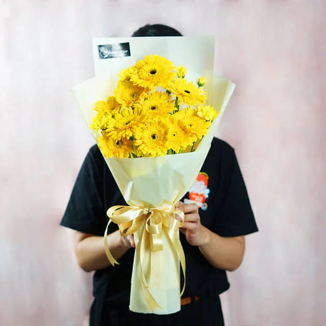 Hand holding a bouquet of fresh yellow gerbera daisies for flower delivery