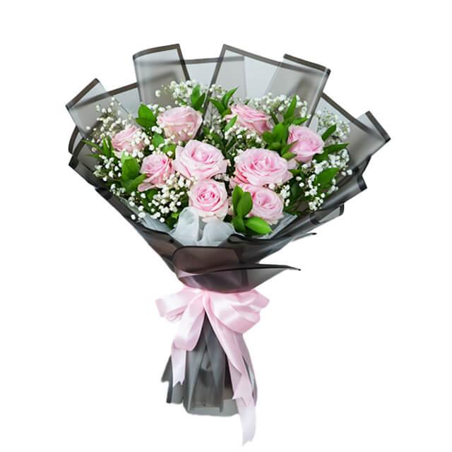 Flower delivery bouquet with pink roses, baby's breath, and greenery wrapped in black with ribbon