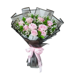 Flower delivery bouquet with pink roses, baby's breath, and greenery wrapped in black with ribbon