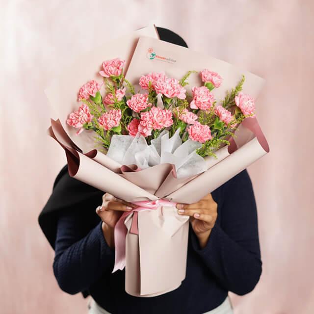 Hand holding pink carnation bouquet with greenery, perfect for flower delivery in Singapore