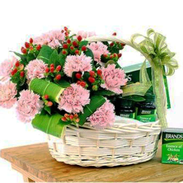 Flower delivery basket with pink carnations, red berries, greenery, and wellness hamper items