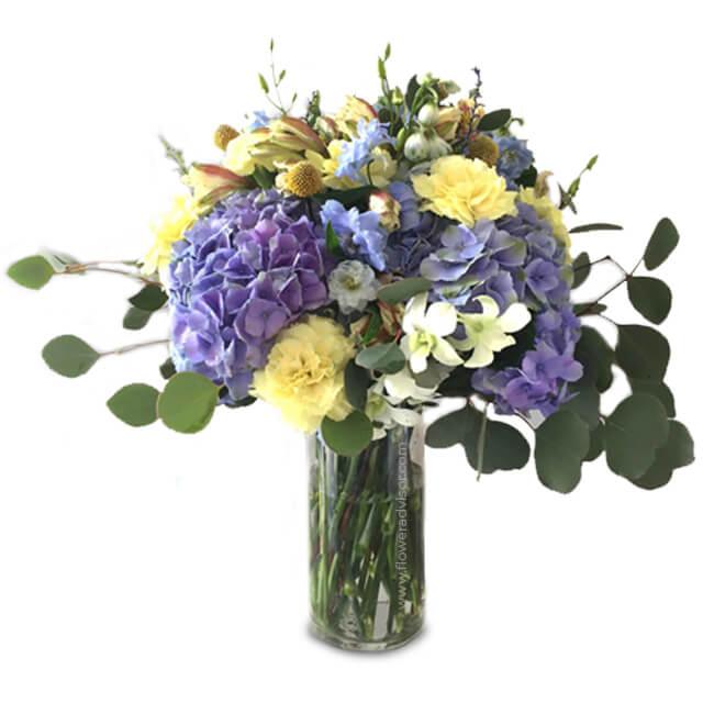 Elegant flower bouquet with hydrangeas and yellow carnations in a glass vase for delivery