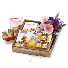 Flower delivery hamper with fresh pastel bouquet, gourmet snacks, cookies, honey jars, and juice