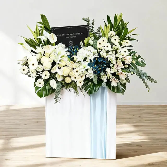 Elegant white and blue condolence flower stand with lilies, gerberas, and orchids for flower delivery