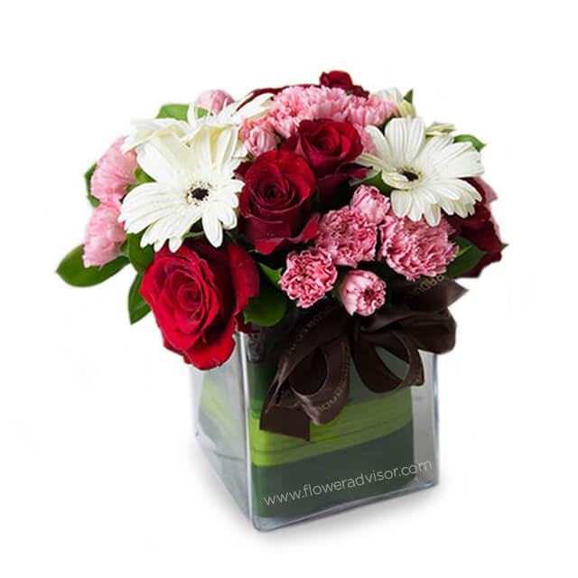Fresh flower delivery of mixed pink roses, carnations, and white gerberas in a glass vase