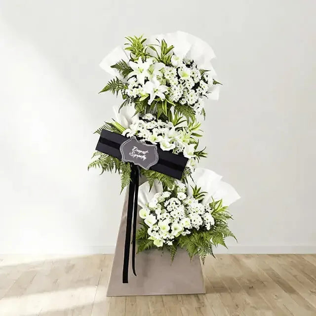 Elegant white funeral flower stand with lilies, chrysanthemums, greenery for delivery