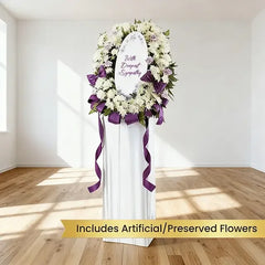 Sympathy flower delivery wreath with white and purple flowers on a stand in bright room