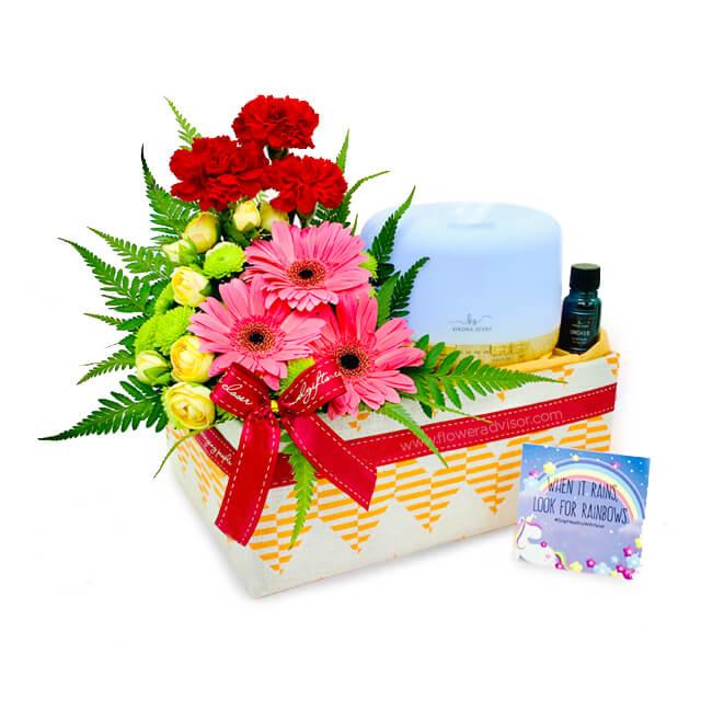 Flower delivery gift basket with pink gerberas, yellow roses, red carnations, and diffuser