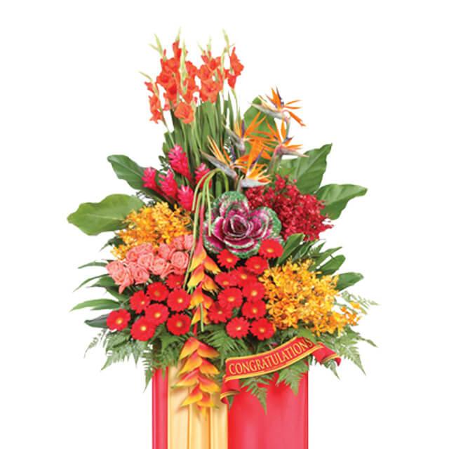 Vibrant congratulatory flower stand with red gerberas, lilies, and lush greenery for delivery