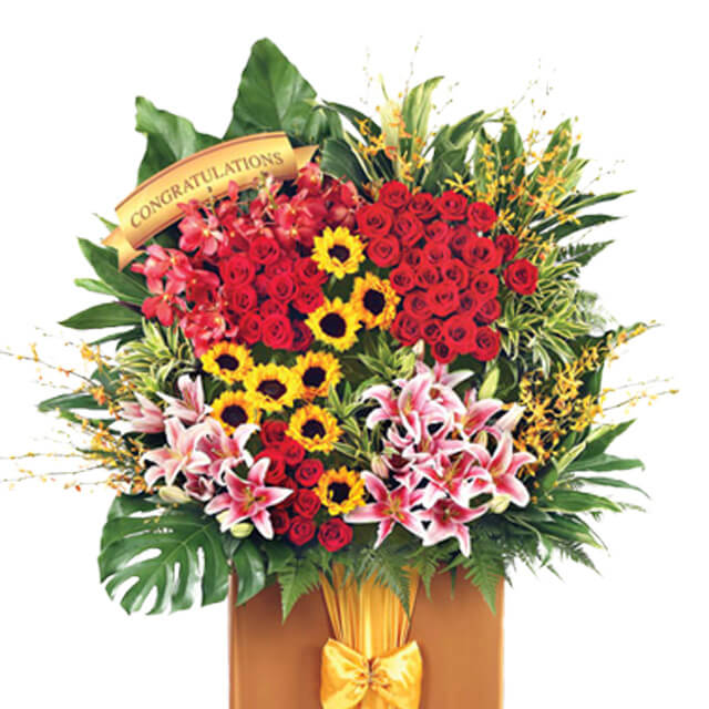 Grand flower arrangement of red roses, sunflowers, lilies and orchids with congratulations ribbon, ideal for flower delivery