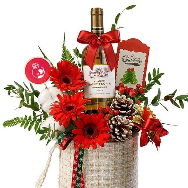Christmas flower delivery arrangement with red gerbera, pinecones, and wine bottle