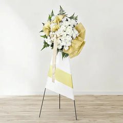 Elegant white floral wreath with gold ribbon on stand for flower delivery in Singapore