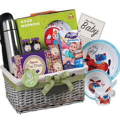 Flower delivery hamper with baby gift items, snacks, plates, and a thermos in a basket