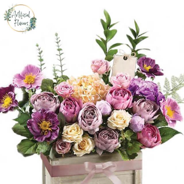 Artificial flower arrangement with mixed pastel roses and blooms in wooden box for delivery