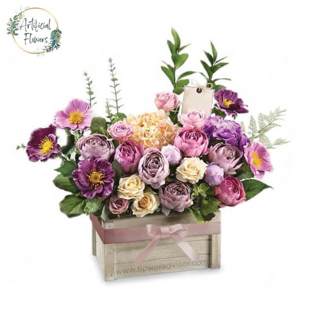 Artificial flower arrangement in pastel shades in a wooden box, ideal for flower delivery