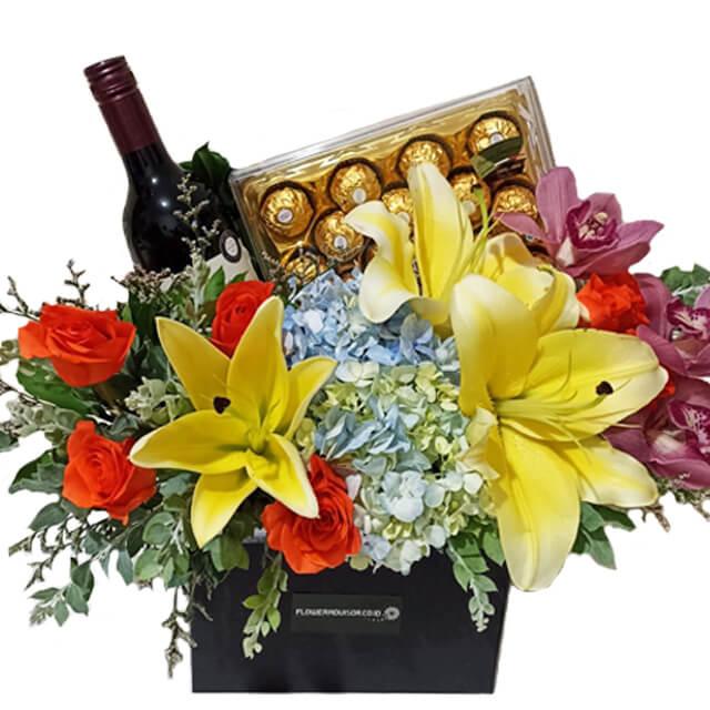 Flower delivery arrangement with yellow lilies, roses, orchids, wine and chocolates