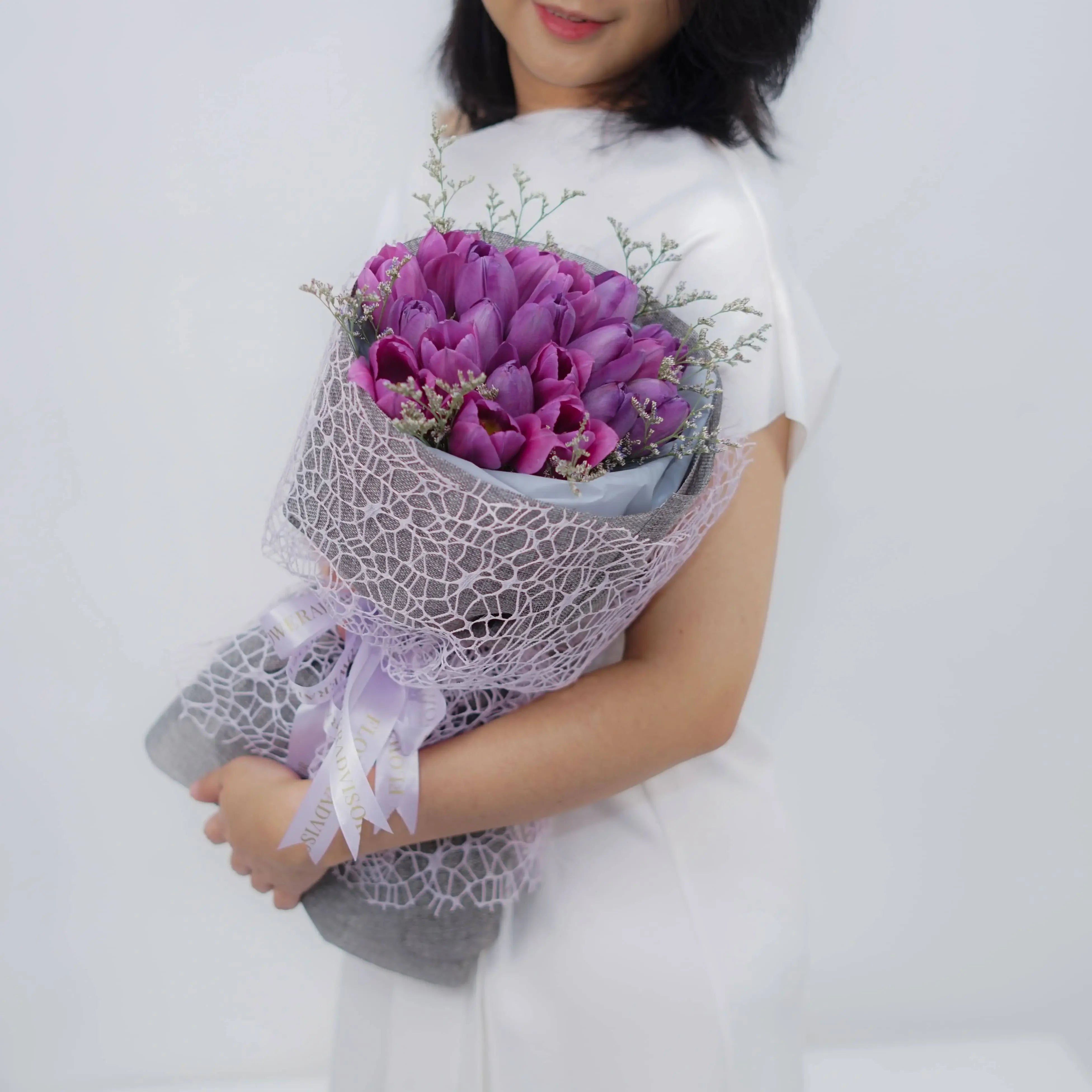 Purple tulip bouquet for flower delivery, wrapped in lace, held by woman in white dress