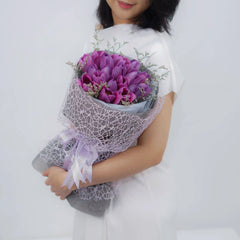 Purple tulip bouquet for flower delivery, wrapped in lace, held by woman in white dress