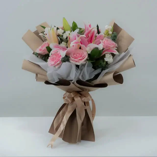 Elegant bouquet of pink lilies and roses for flower delivery, wrapped in brown paper with ribbon
