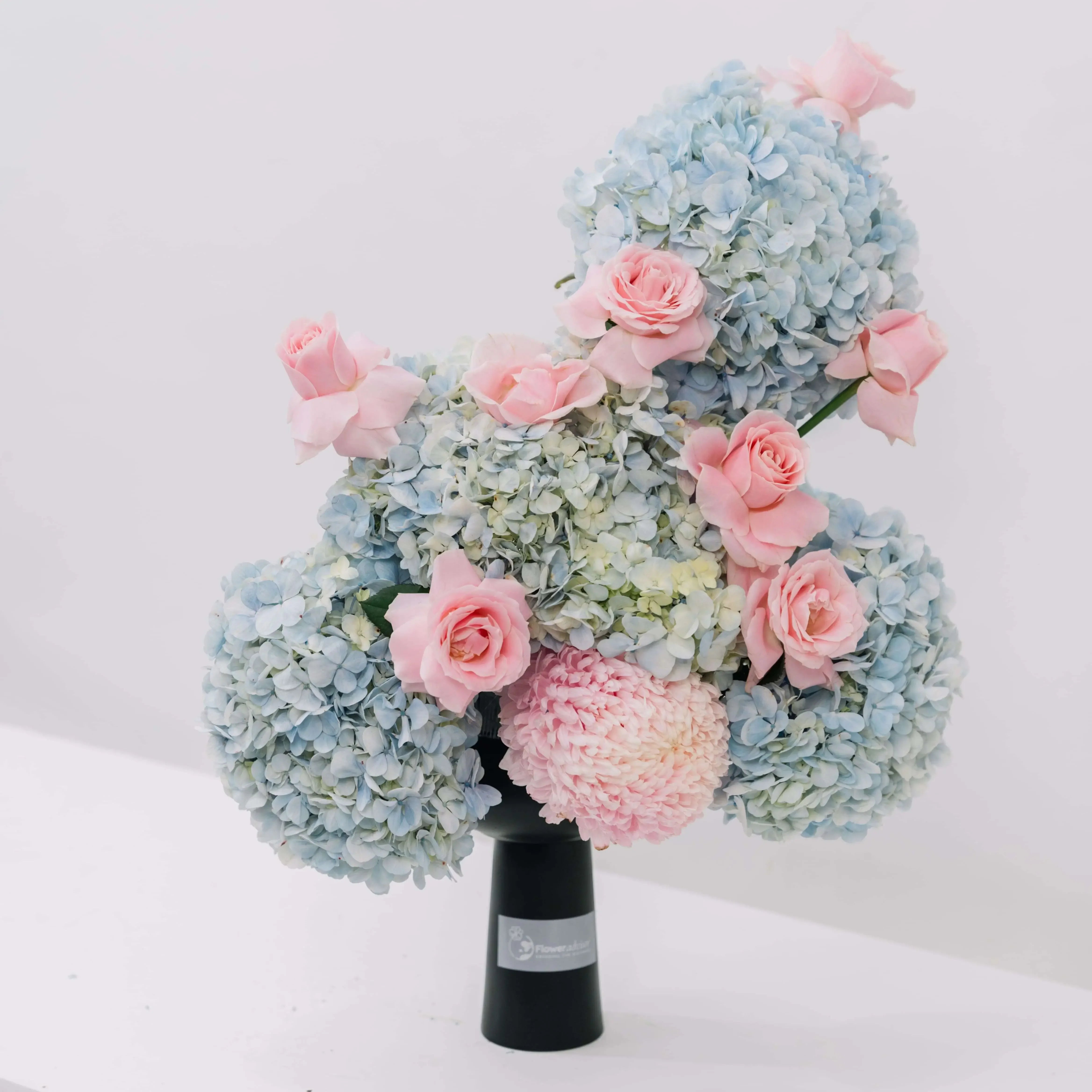 Blue hydrangeas and pink roses bouquet in a black vase for flower delivery