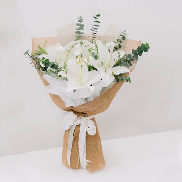 Elegant white lily bouquet with greenery, wrapped in burlap, ideal for flower delivery