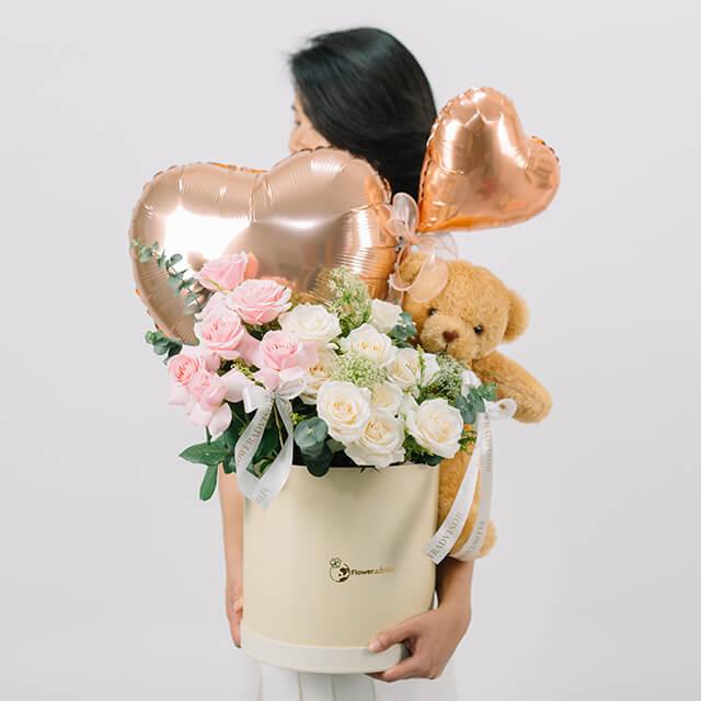 Flower delivery with pink and white roses, heart balloons, and teddy bear in a gift box