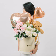 Flower delivery with pink and white roses, heart balloons, and teddy bear in a gift box