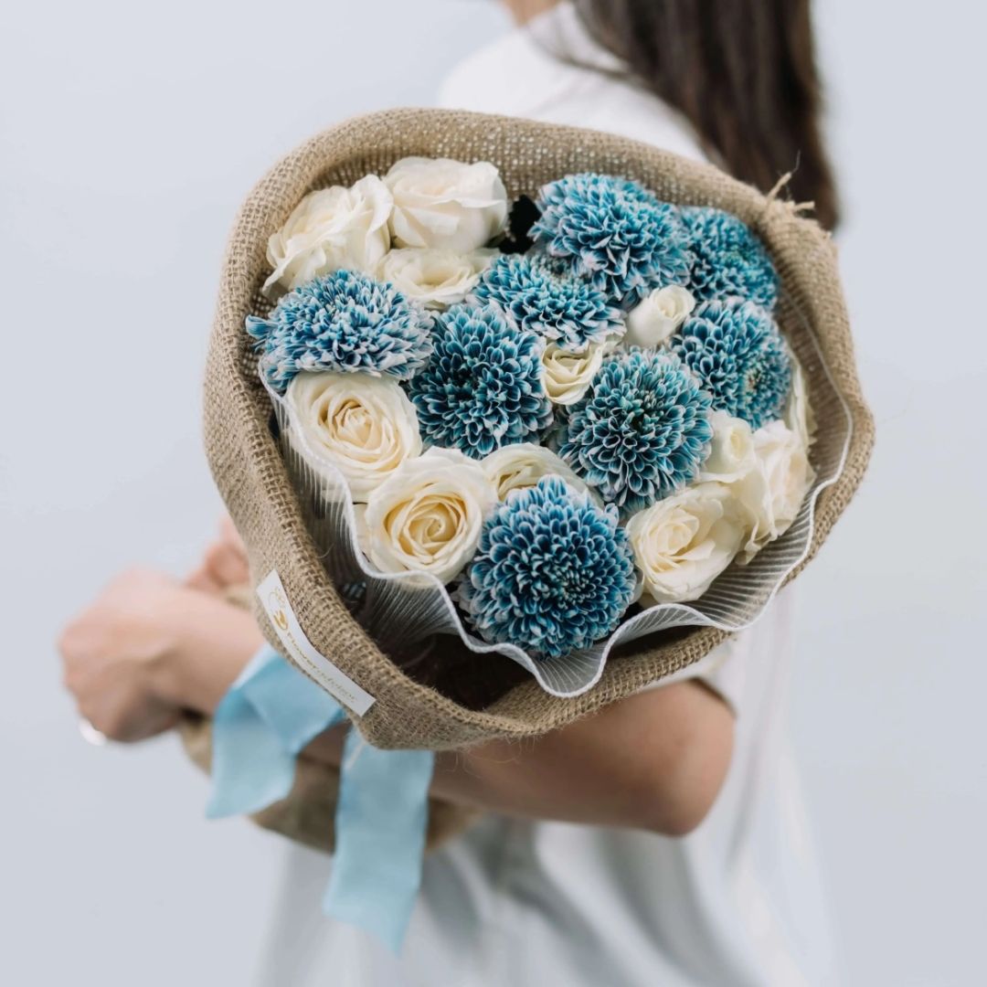 Hand holding a bouquet of blue chrysanthemums and white roses for flower delivery