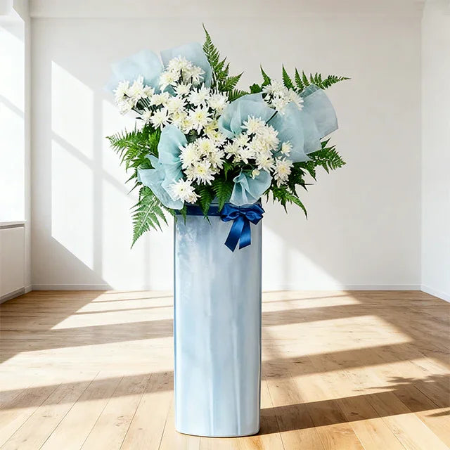 White flower arrangement with ferns and blue wrapping, perfect for Singapore flower delivery