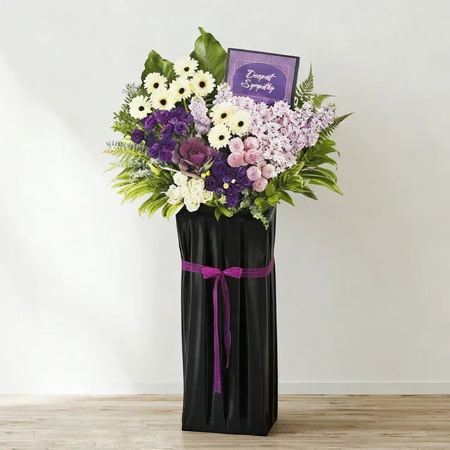 Sympathy flower stand with purple, white and pink blooms for delivery