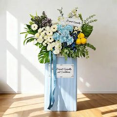 Sympathy flower stand with white, blue, and yellow flowers for condolence delivery