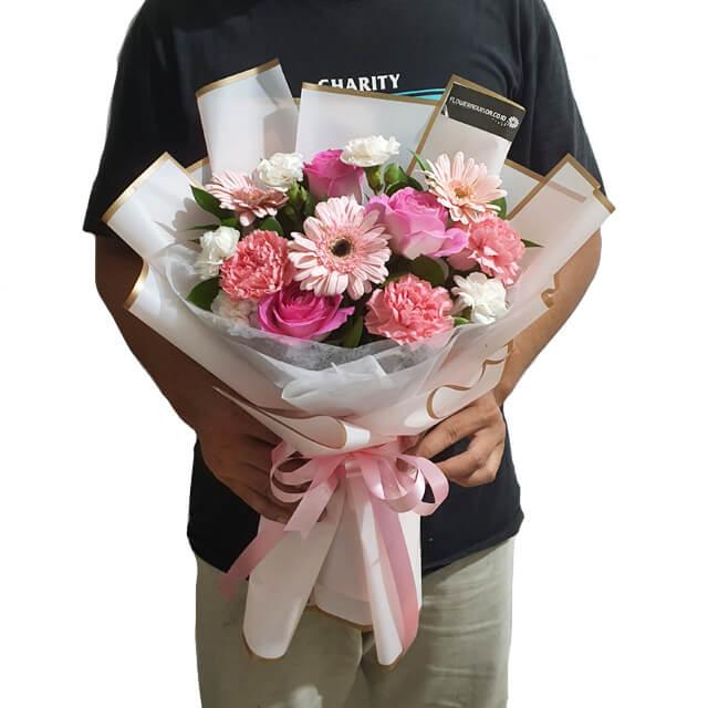 Hand holding a fresh pink flower bouquet with carnations and gerberas for delivery